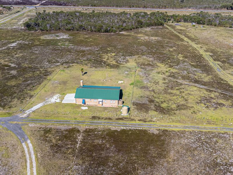 Aerial view of a rural farm property featuring a brick dwelling with a green metal roof, water storage tanks, and expansive surrounding land.