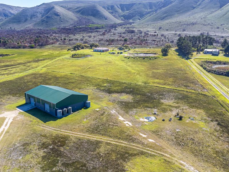 Aerial view of a large farm property featuring a substantial metal shed, water storage tanks, and expansive open grazing land with mountain views.