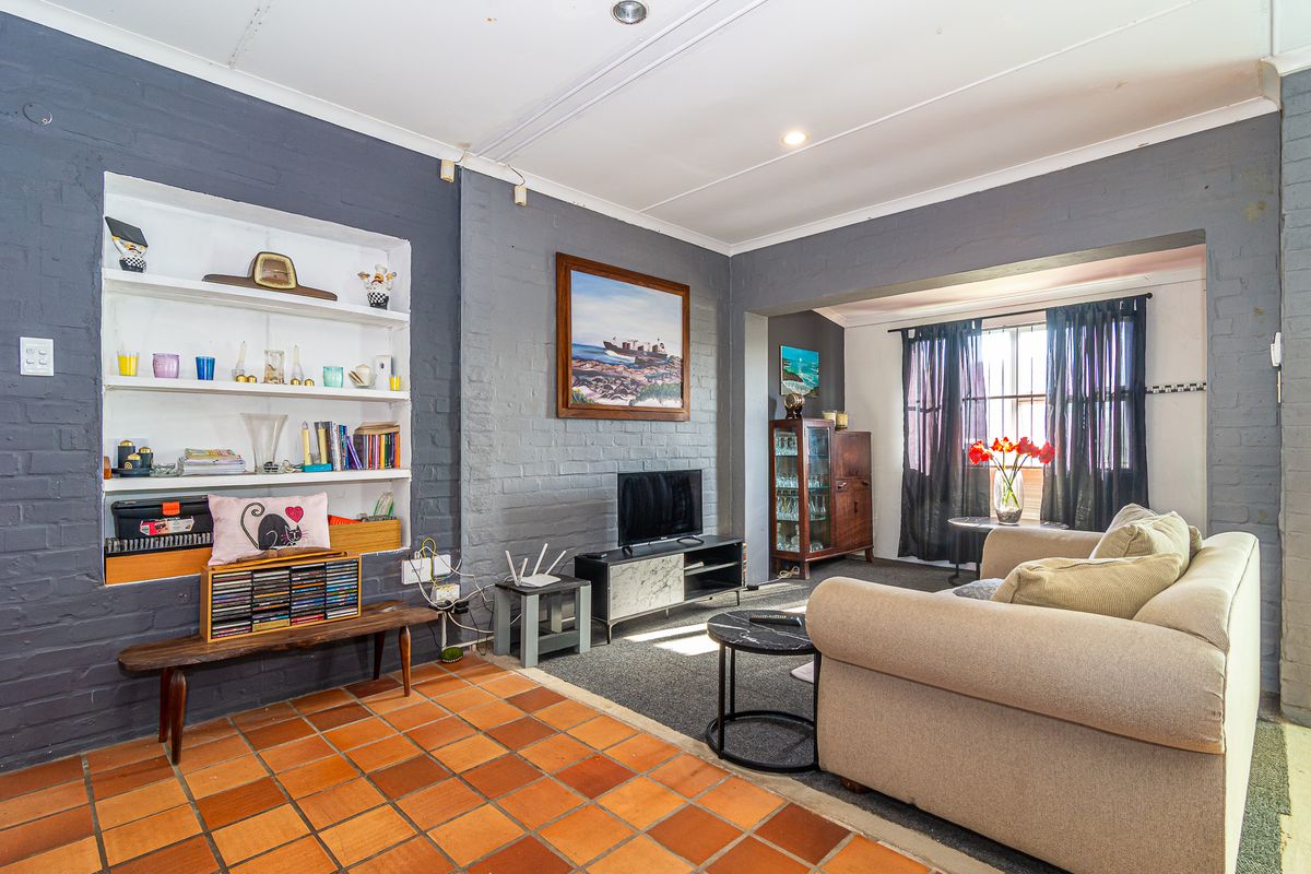 A living room featuring painted brick walls, built-in shelving, and terracotta floor tiles, offering a cozy space with potential for modern updates.