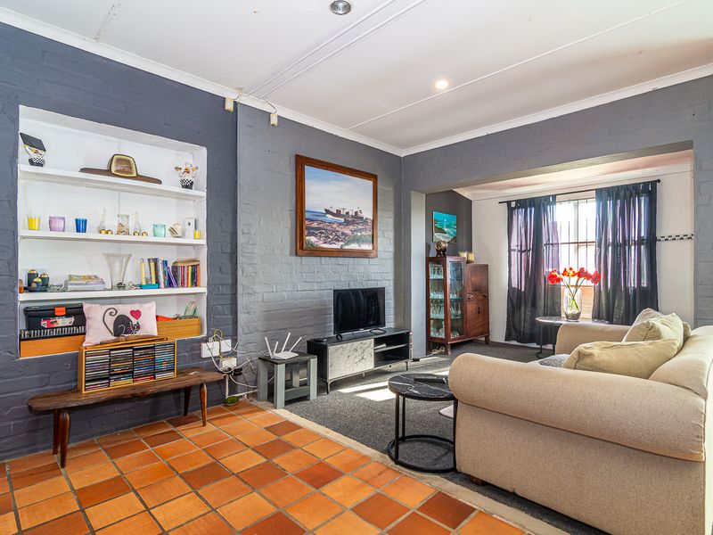 A living room featuring painted brick walls, built-in shelving, and terracotta floor tiles, offering a cozy space with potential for modern updates.