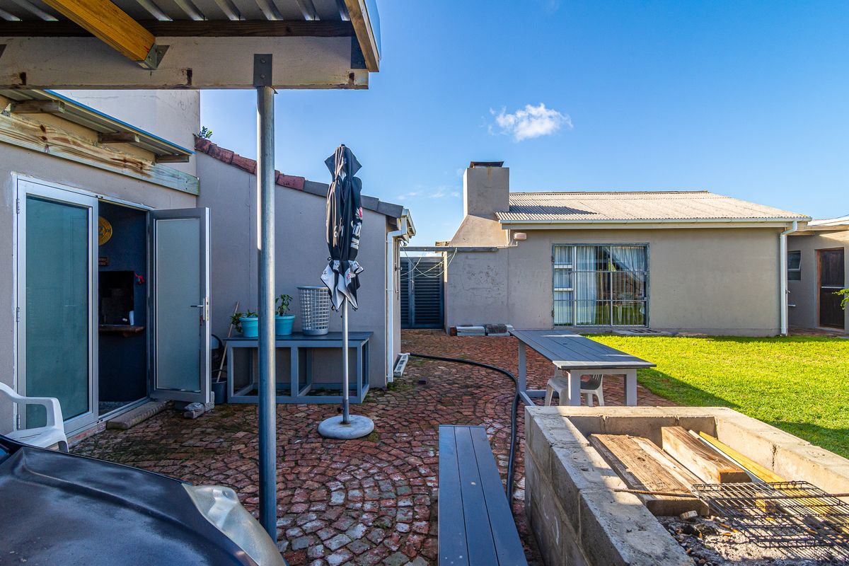 Rear exterior view featuring a brick-paved patio, a built-in braai area, and a covered section, providing a functional outdoor space for entertaining.