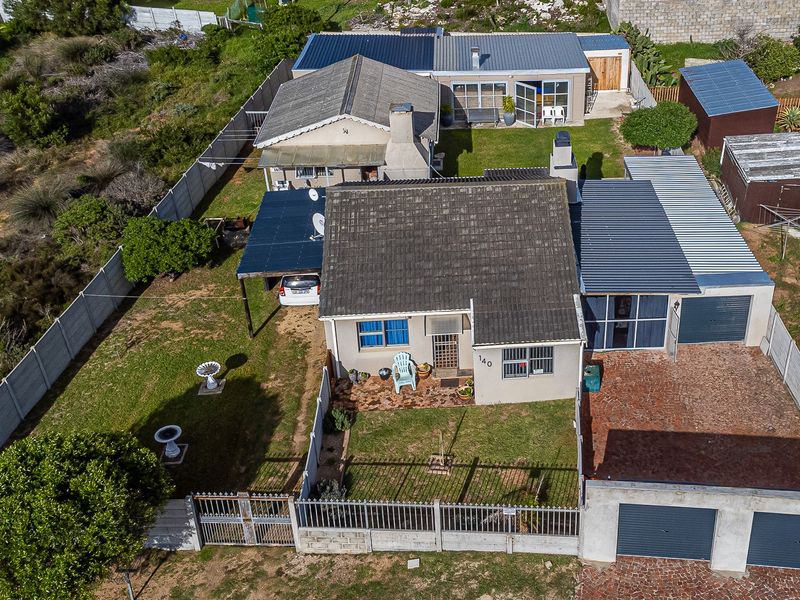 Aerial view of a residential property featuring a main house with tiled roof, a detached garage, brick driveway, and a fenced garden area.