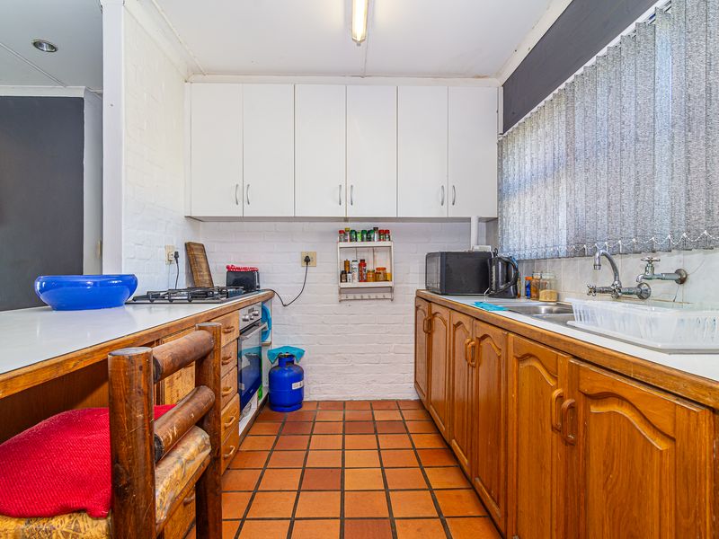 A functional kitchen featuring wooden cabinetry, a gas hob, built-in oven, and tiled flooring, offering a classic layout with potential for modern updates.