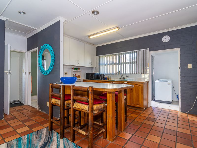 A dated kitchen featuring wooden cabinetry, tiled flooring, and an adjacent laundry area, offering significant potential for a modern renovation.