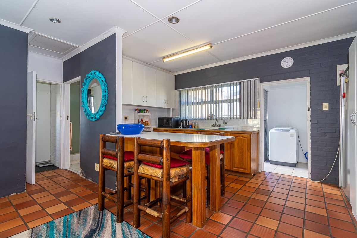 A dated kitchen featuring wooden cabinetry, tiled flooring, and an adjacent laundry area, offering significant potential for a modern renovation.