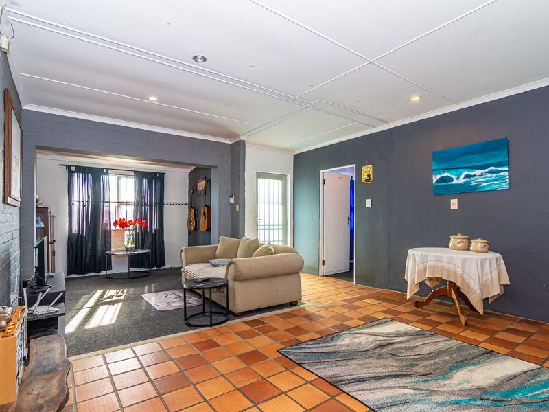 Spacious living area featuring terracotta tile flooring, recessed lighting, and dark-toned walls, offering a versatile layout with potential for modern updates.