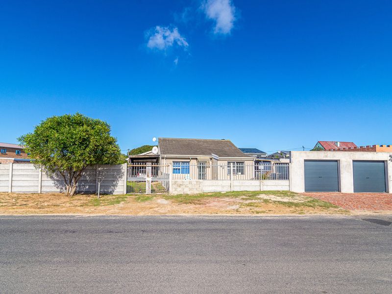 Front exterior view of a single-story house featuring a double garage, paved driveway, and secure boundary wall with metal gate.