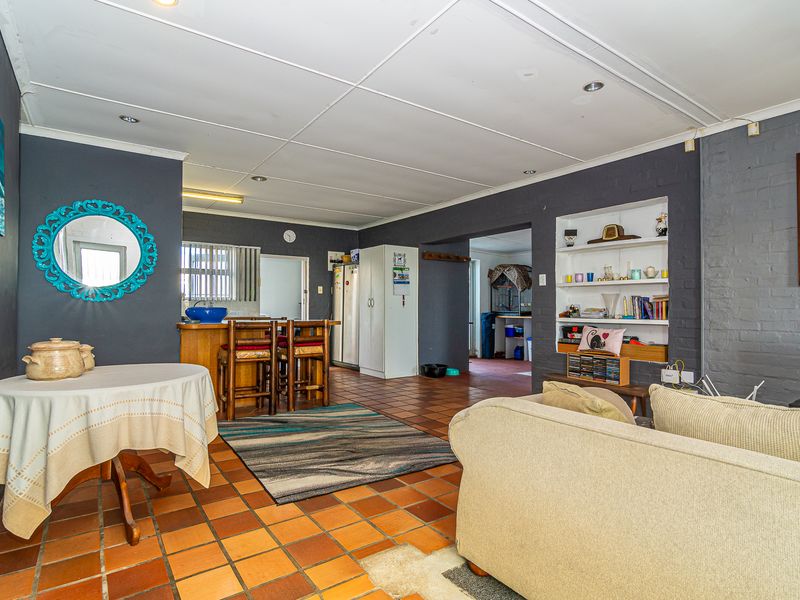 Open plan living and dining area featuring terracotta tile flooring, built-in shelving, and a breakfast bar with a dark painted brick accent wall.