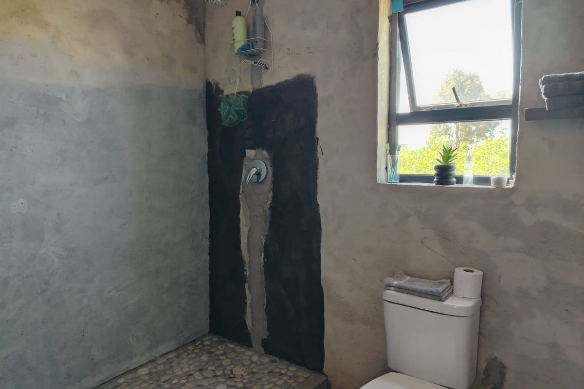 Bathroom featuring a pebble-floored shower area and toilet, currently in an unfinished state with exposed plaster and waterproofing.