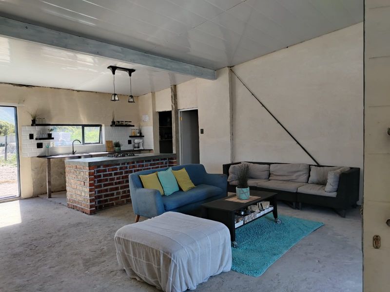 Open-plan living and kitchen area featuring an exposed brick island, subway tile backsplash, and industrial-style concrete flooring with unfinished wall textures.