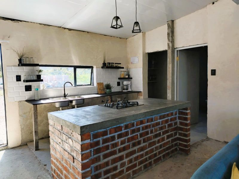 Industrial-style kitchen featuring an exposed brick island with a concrete countertop, gas hob, and subway tile backsplash, currently in an unfinished state.