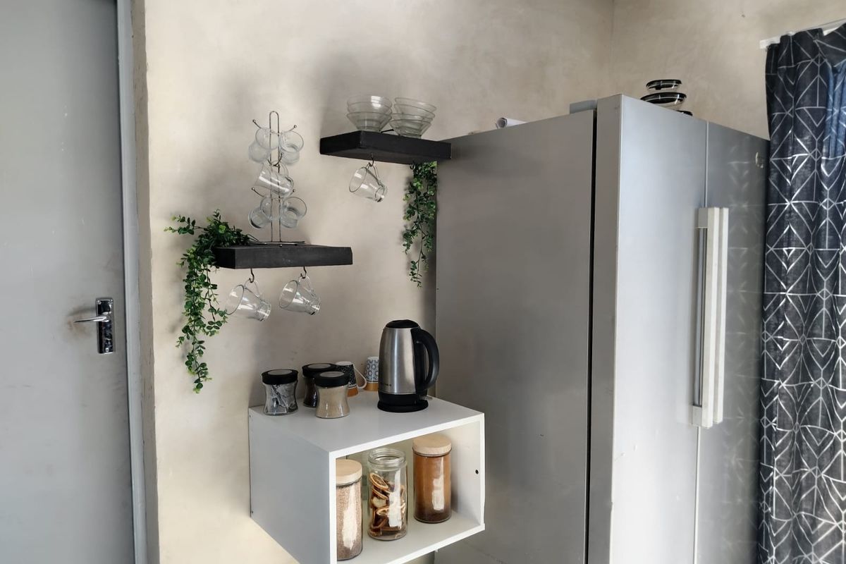 A kitchen corner featuring floating shelves and a wall-mounted storage unit, providing functional storage space alongside a refrigerator.