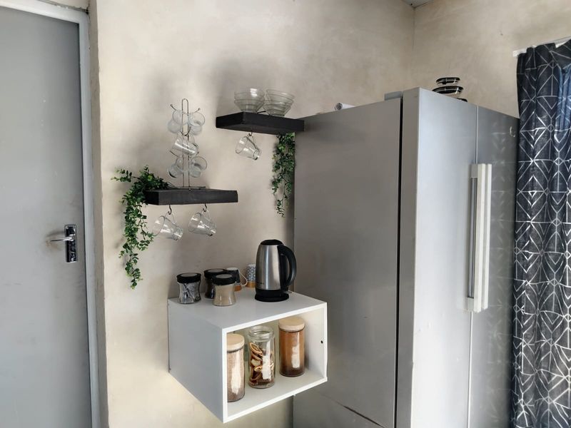A kitchen corner featuring floating shelves and a wall-mounted storage unit, providing functional storage space alongside a refrigerator.