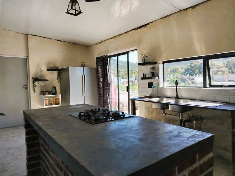 Rustic kitchen featuring a central island with a gas cooktop, double sink, and subway tile backsplash, currently requiring finishing touches to the walls and plumbing.