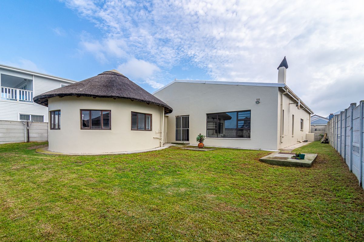 Rear view of the property featuring a unique circular structure with a thatched roof, a chimney, and a spacious grass garden area.