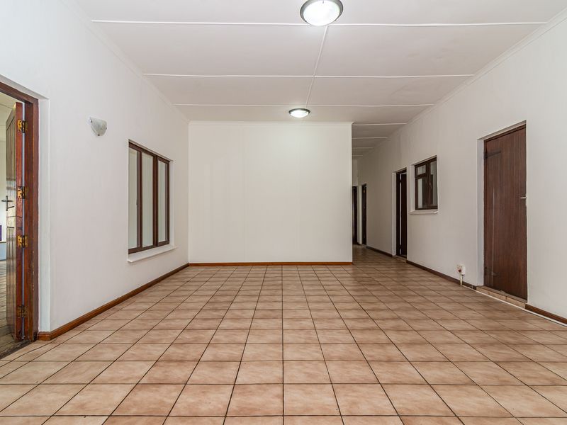 A spacious, empty hallway featuring neutral tiled flooring, white walls, and multiple wooden door frames leading to adjacent rooms.