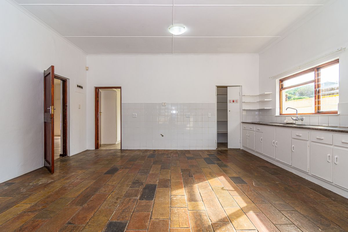 An empty, dated kitchen featuring terracotta floor tiles, white cabinetry, a tiled backsplash, and a separate pantry area.