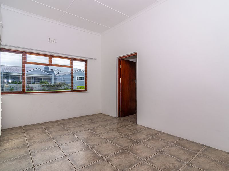 A clean, empty bedroom featuring tiled flooring, built-in cupboards, and a large window providing natural light.