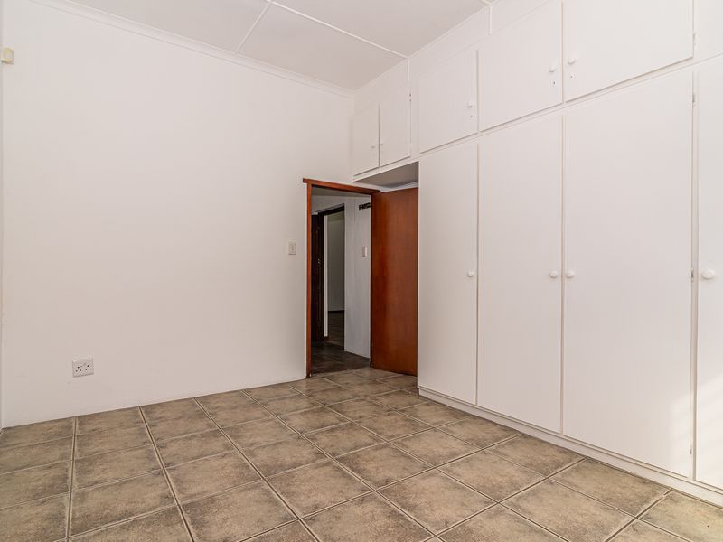 An empty bedroom featuring neutral tiled flooring and extensive white built-in cupboards providing ample storage space.