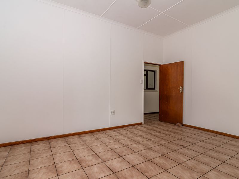 An empty bedroom featuring tiled flooring, white wall panels, and a wooden door, providing a blank canvas for potential interior design updates.