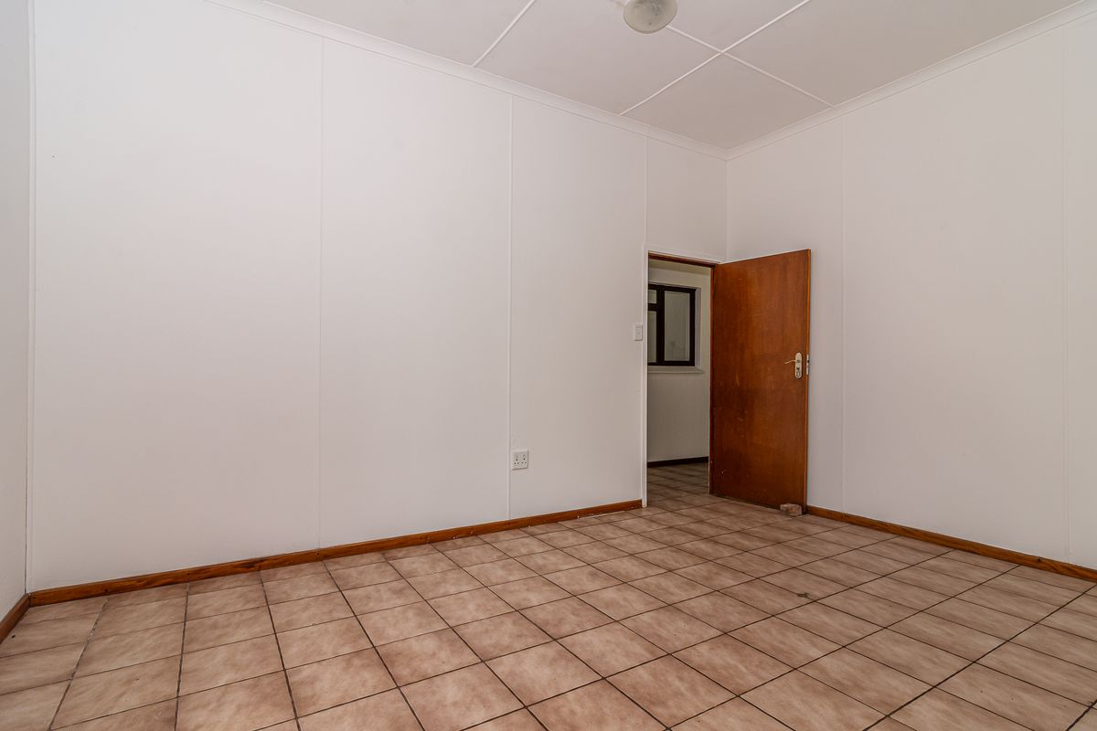 An empty bedroom featuring tiled flooring, white wall panels, and a wooden door, providing a blank canvas for potential interior design updates.