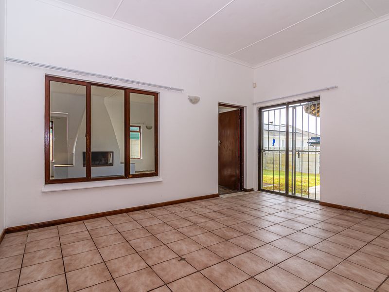 An empty living room featuring tiled flooring, an internal window, and a sliding glass door with a security gate leading to the exterior.