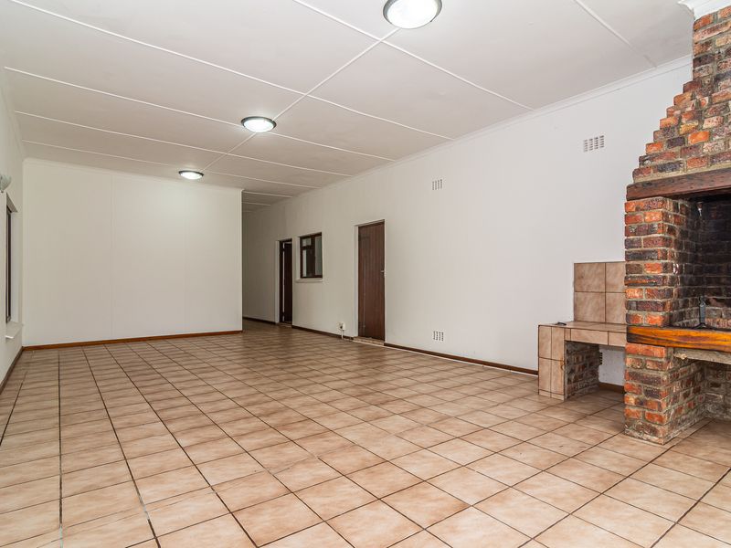 Spacious living area featuring a prominent built-in brick fireplace and neutral tiled flooring, offering a versatile blank canvas for interior design.