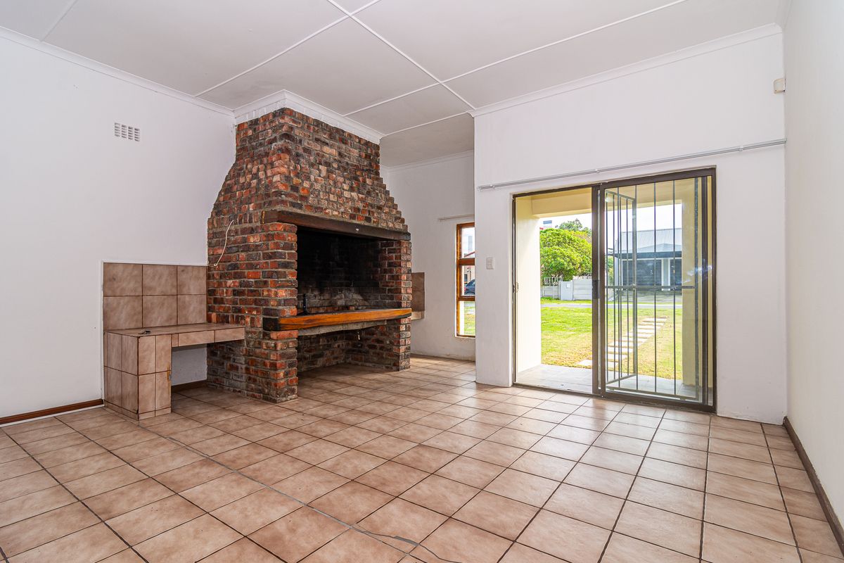 Spacious living area featuring a large built-in brick fireplace, tiled flooring, and direct access to the garden through sliding glass doors.