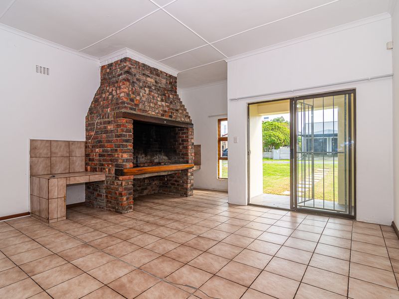 Spacious living area featuring a large built-in brick fireplace, tiled flooring, and direct access to the garden through sliding glass doors.