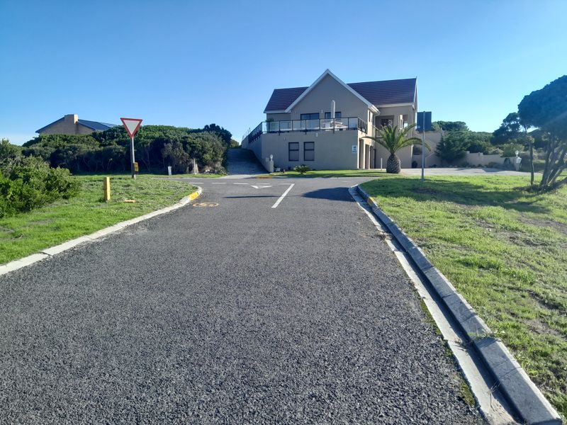 A street-level view of the property entrance, featuring an asphalt driveway leading to a multi-story residential building with a tiled roof and balcony.