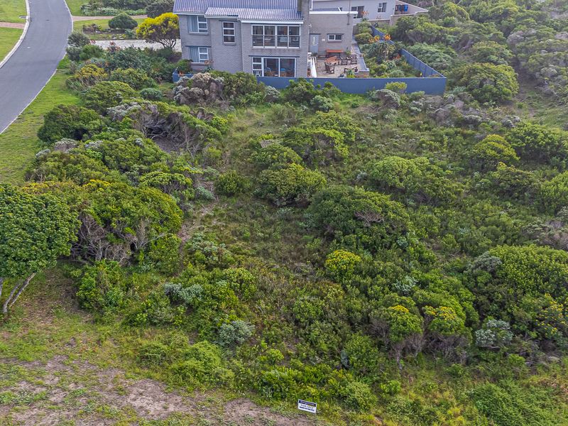 An aerial view of a vacant residential plot covered in native coastal vegetation, situated adjacent to an existing residential property and paved road.
