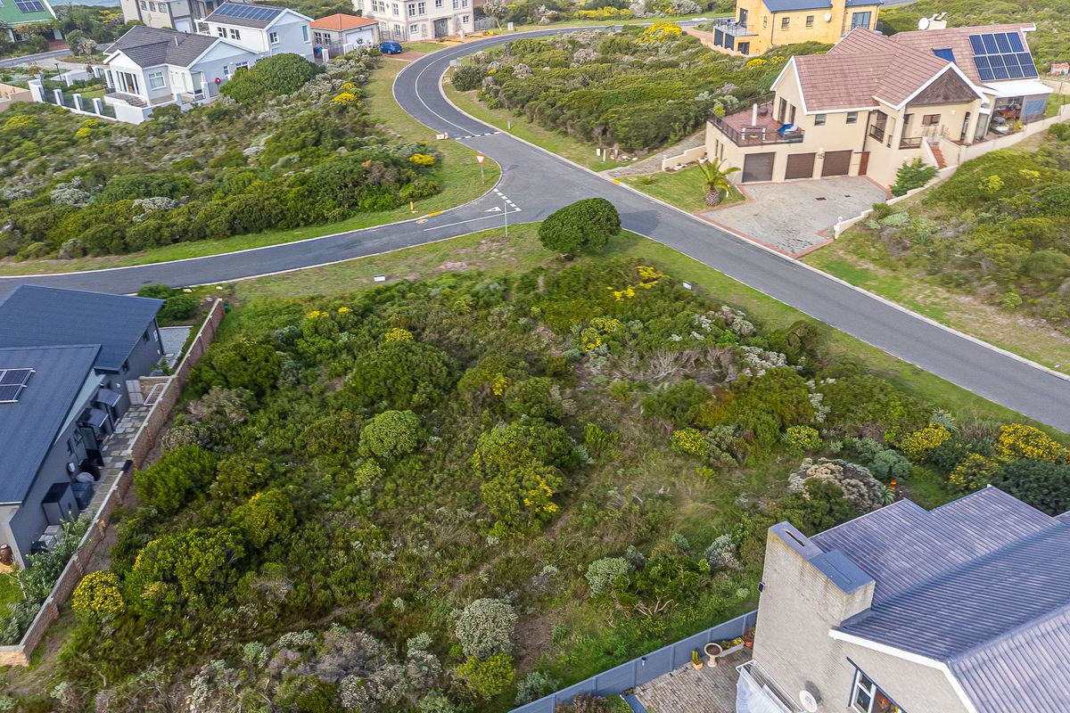 An aerial view of a vacant residential plot covered in native vegetation, situated within an established coastal neighborhood.