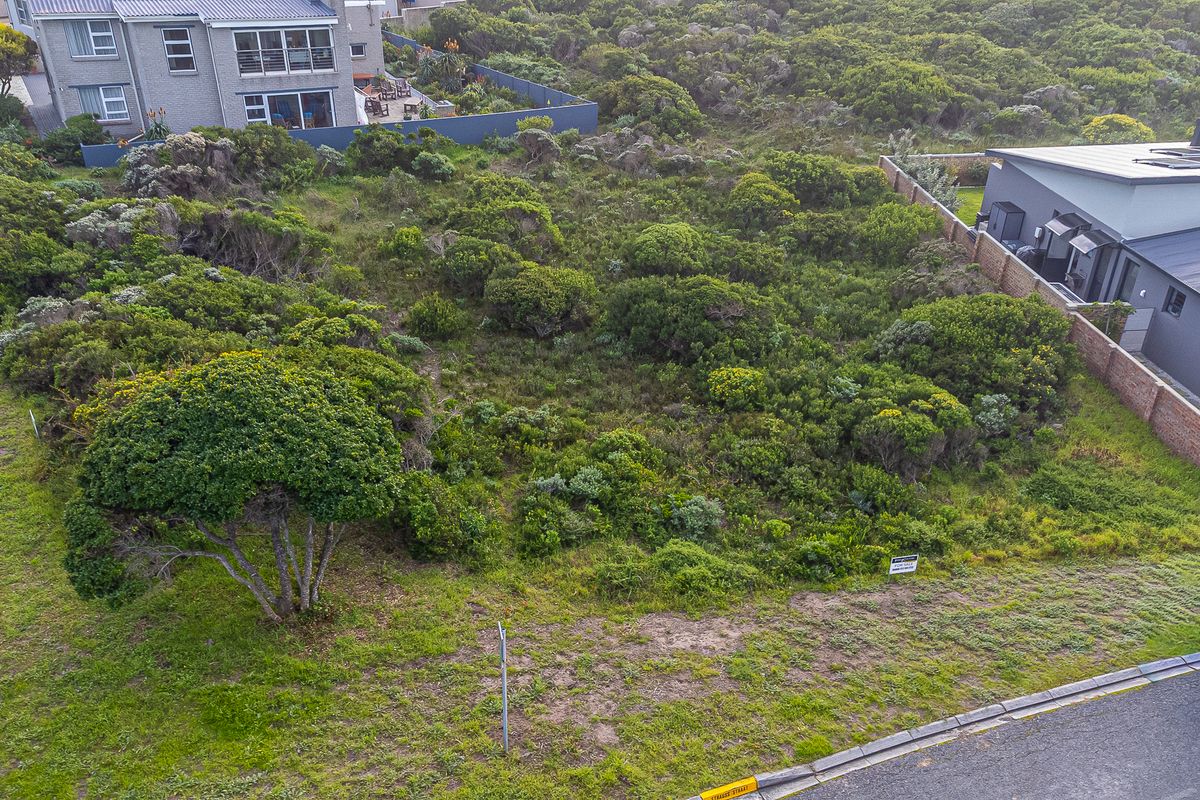 An aerial view of a vacant residential plot featuring native vegetation, bordered by existing residential properties and a boundary wall.