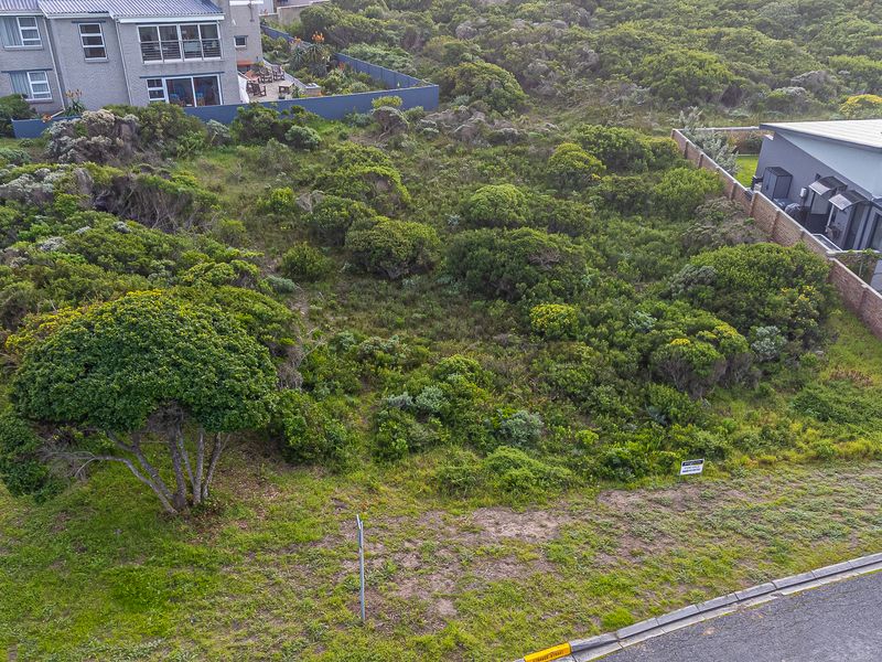 An aerial view of a vacant residential plot featuring native vegetation, bordered by existing residential properties and a boundary wall.