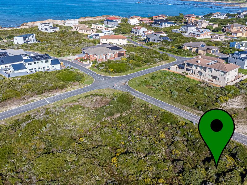 Aerial view of a vacant residential plot situated in a coastal neighborhood with established road infrastructure and surrounding homes.