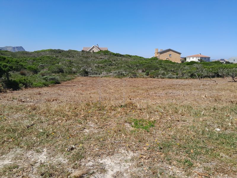 A view of a vacant residential plot featuring natural coastal vegetation and surrounding neighborhood homes.
