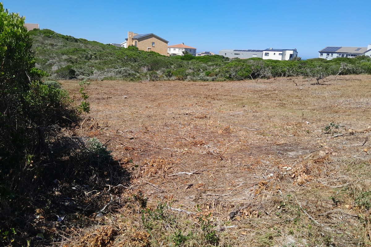 A vacant residential plot of land featuring natural coastal vegetation and surrounding neighborhood views.