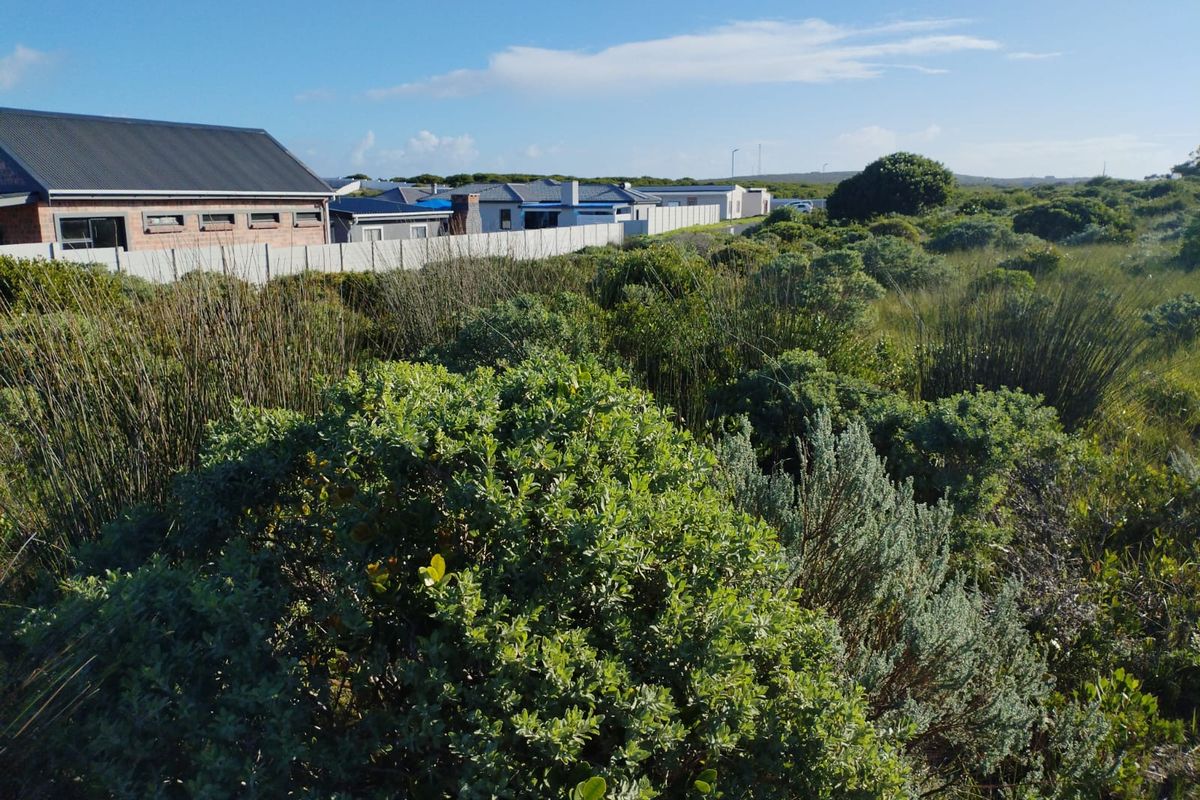 A view of a vacant residential plot featuring natural coastal vegetation and perimeter fencing, adjacent to established residential properties.