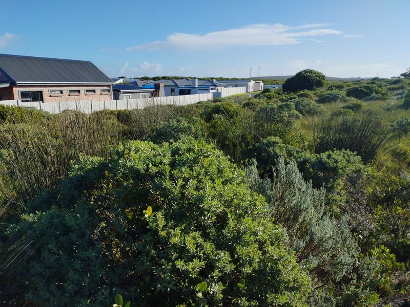 A view of a vacant residential plot featuring natural coastal vegetation and perimeter fencing, adjacent to established residential properties.