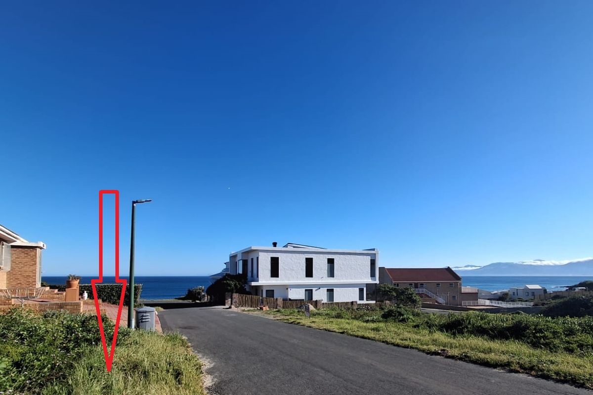 A street view of the residential area showing the road, coastal surroundings, and nearby properties under a clear blue sky.