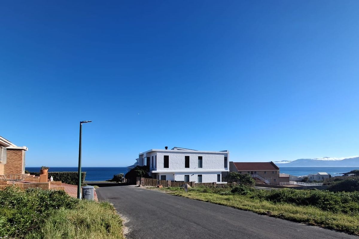 A clear street view of a coastal residential area featuring paved roads, surrounding homes, and scenic ocean views in the background.