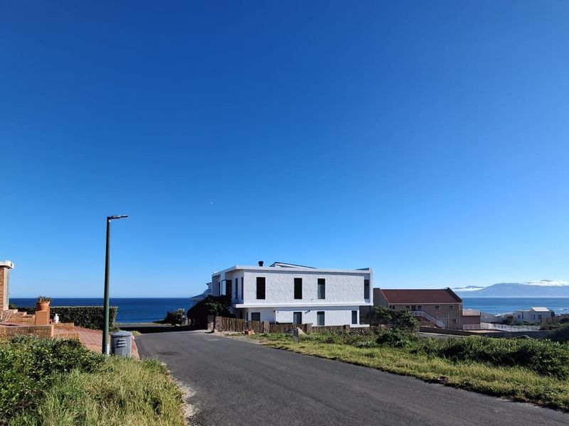 A clear street view of a coastal residential area featuring paved roads, surrounding homes, and scenic ocean views in the background.