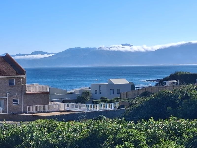 A scenic elevated view overlooking the coastline, ocean, and distant mountain range, showcasing the property's prime coastal location.