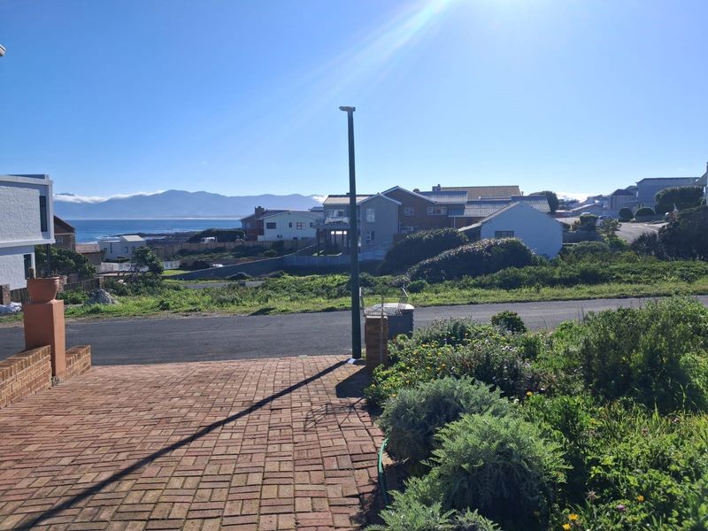 A scenic view overlooking the neighbourhood with distant mountain and ocean vistas, featuring a paved driveway and established garden area.