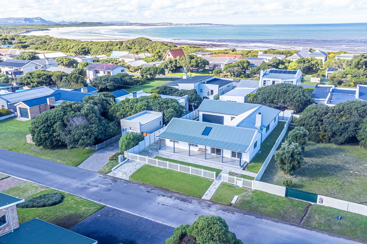 Aerial view of a coastal residential property featuring a metal roof, paved driveway, and a covered patio, situated near the beach.
