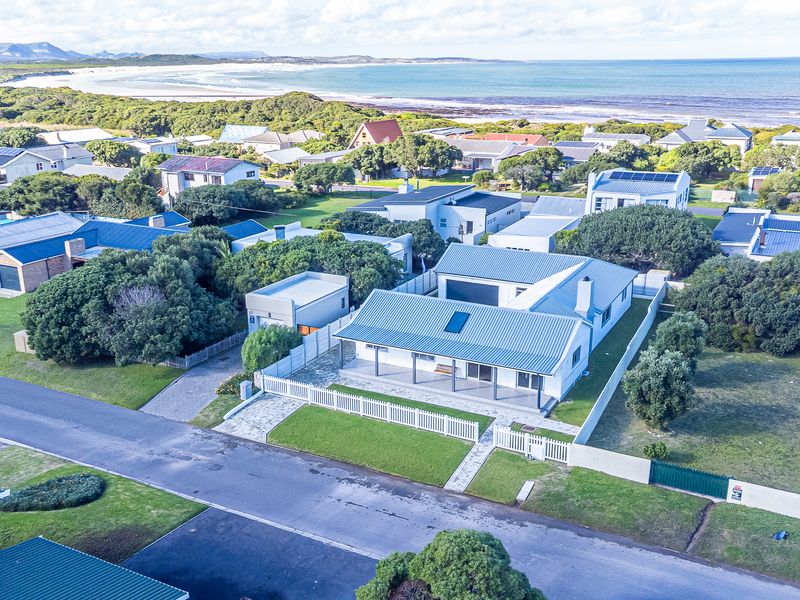 Aerial view of a coastal residential property featuring a metal roof, paved driveway, and a covered patio, situated near the beach.