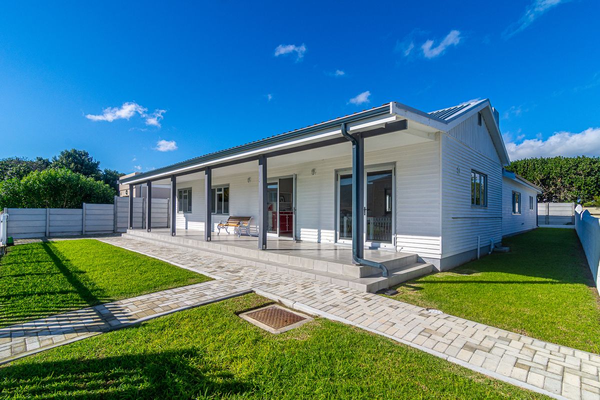 Rear view of the house featuring a spacious covered patio with tiled flooring, sliding glass doors, and a well-maintained garden with paved walkways.