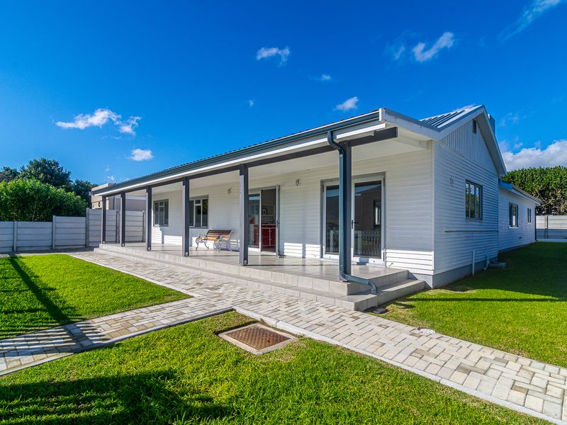 Rear view of the house featuring a spacious covered patio with tiled flooring, sliding glass doors, and a well-maintained garden with paved walkways.