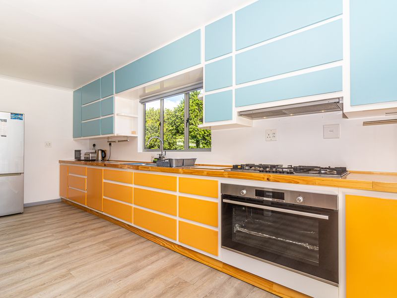 A bright kitchen featuring vibrant blue and orange cabinetry, wooden countertops, a gas hob, built-in oven, and modern laminate flooring.