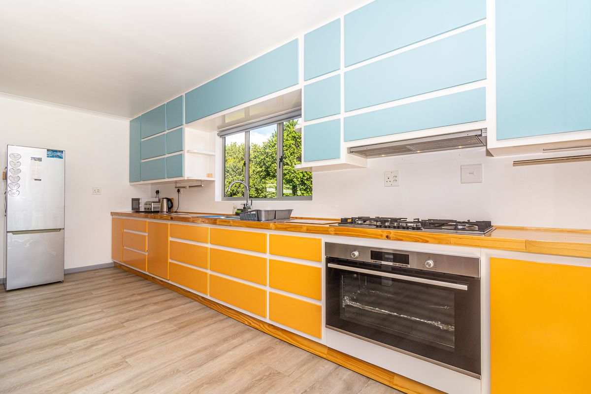 A bright kitchen featuring vibrant blue and orange cabinetry, wooden countertops, a gas hob, built-in oven, and modern laminate flooring.